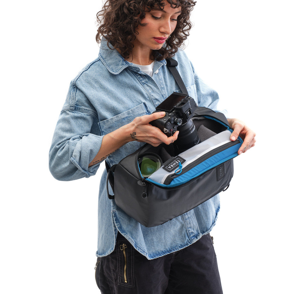 Woman holding a camera and a black and blue bag on a white background