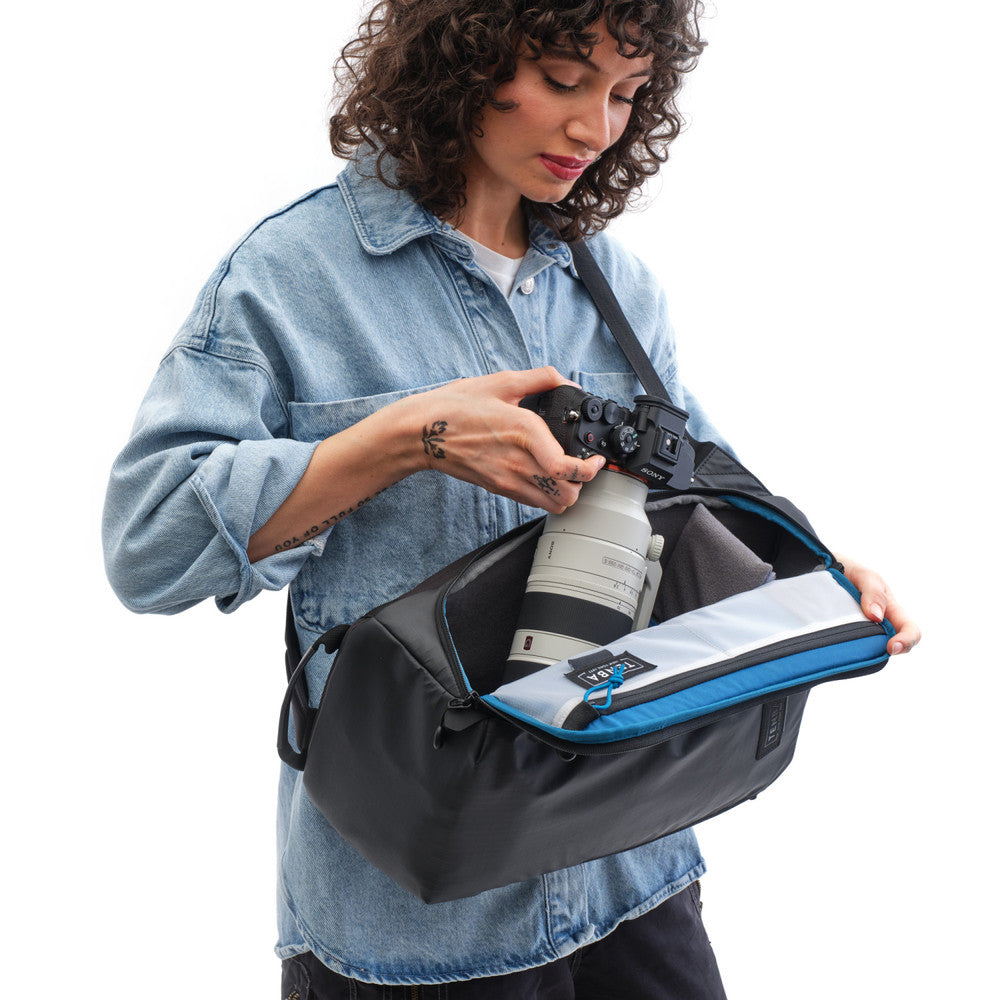 Woman holding a camera bag with a camera inside on a white background