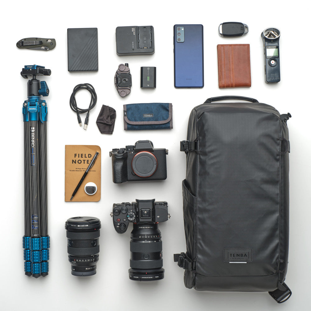Collection of photography and travel gear including a camera, lenses, backpack, and accessories on a white background.