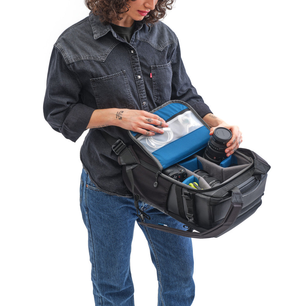 Person holding a large black backpack with compartments, wearing a denim shirt and jeans.