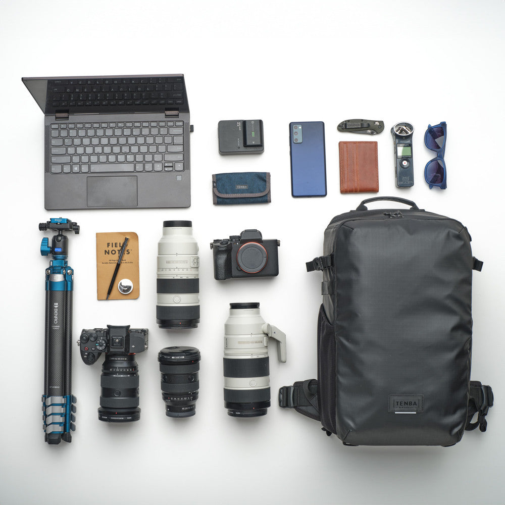 Collection of travel or photography equipment including a laptop, backpack, camera, lenses, and other accessories on a white background.