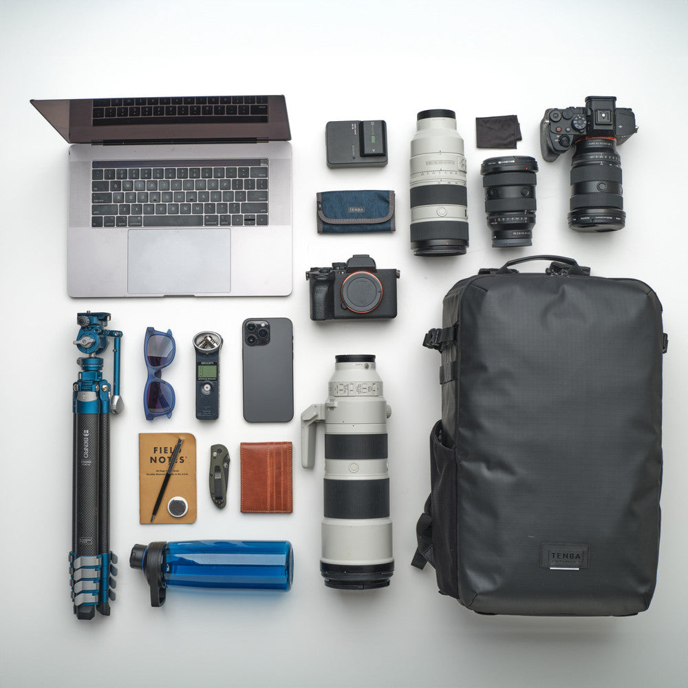 Collection of photography equipment including a laptop, camera, lenses, backpack, and other accessories on a white background.