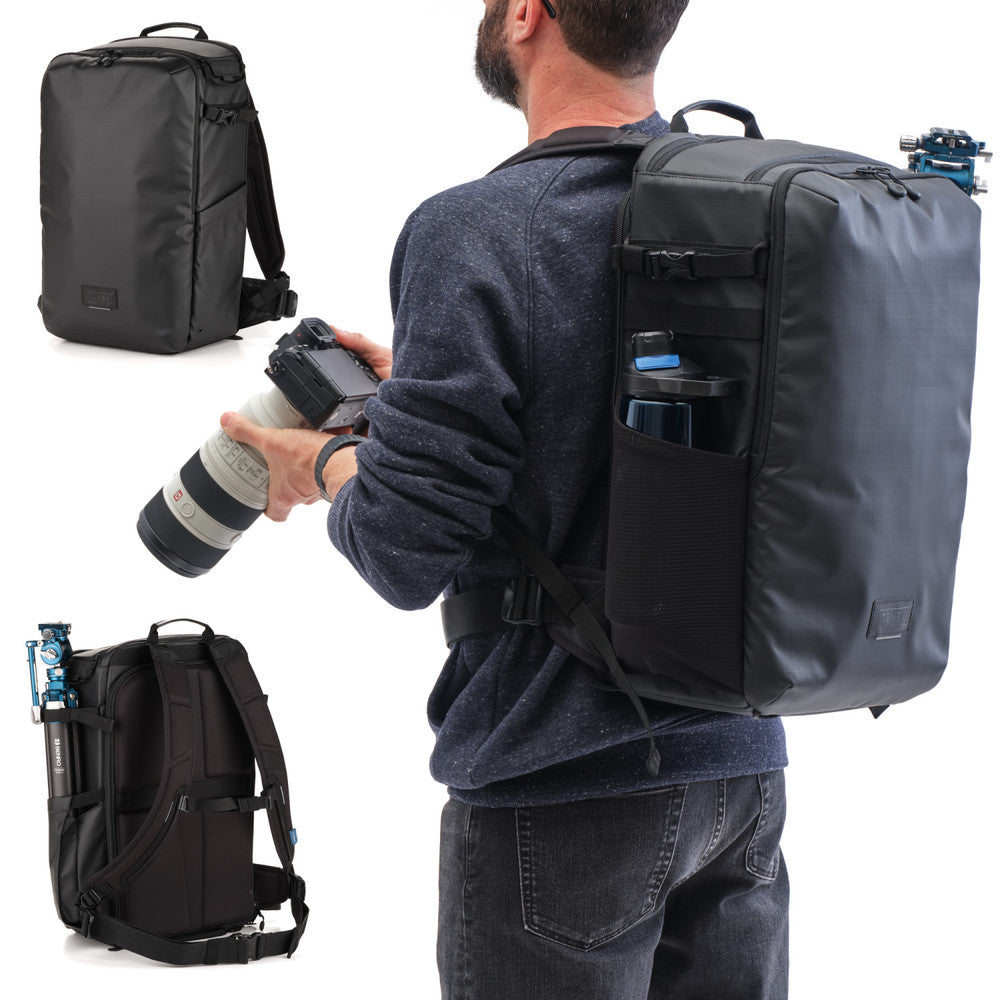 Man with a large black backpack holding a camera, with additional backpacks displayed.