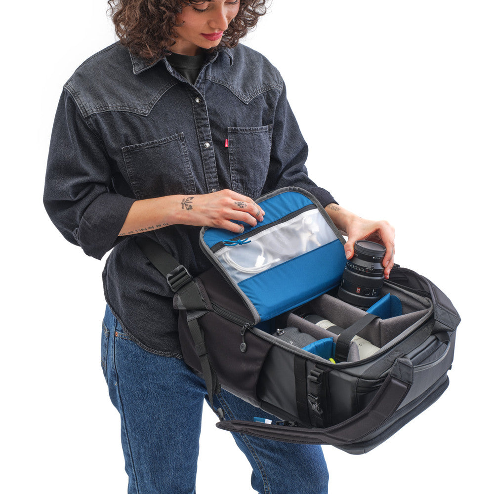 Person opening a large black and blue camera bag with a white background
