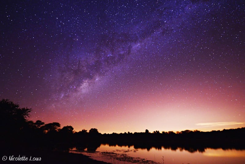 Starscape with purple hue photographed over lake
