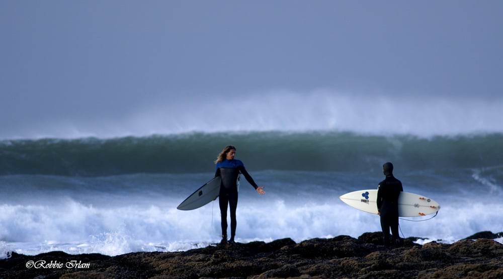 Photograph of one surfer gesturing for the other surfer to join