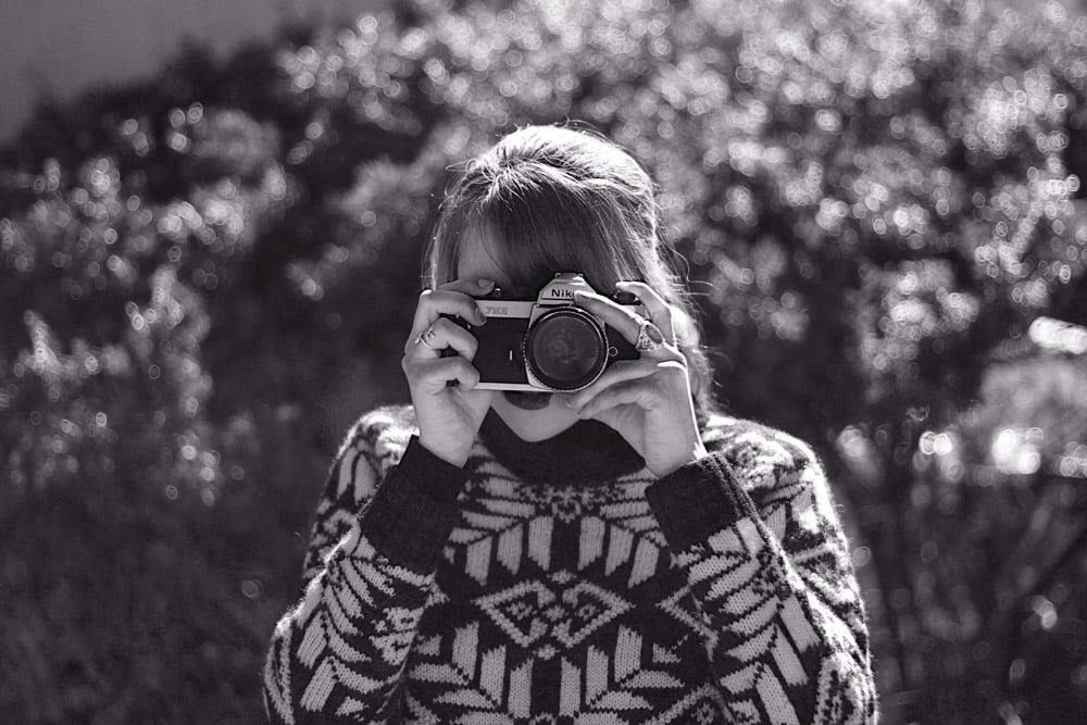 A black and white self portrait by Alison posing with her Nikon Film Camera