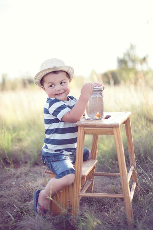 Toddler Photography: Little boy with a hat on his head, sitting on a stepping-stool holding a console jar with a goldfish inside.