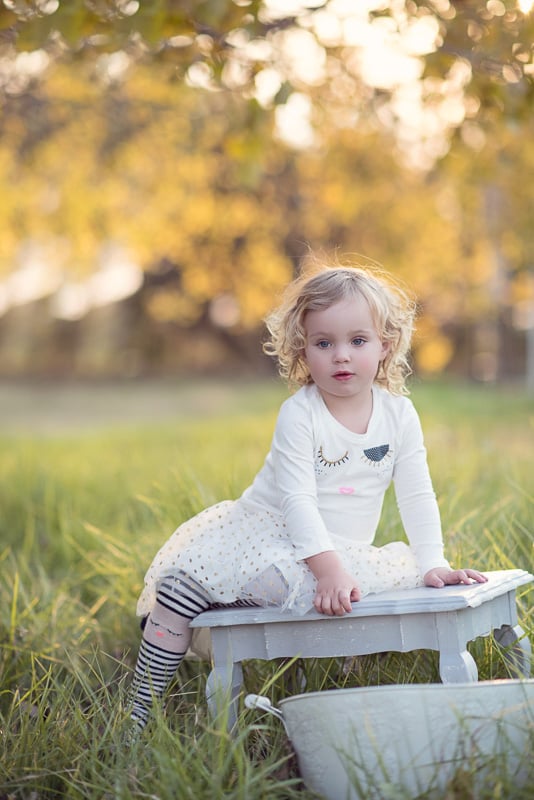 Toddler Photography: Little girl sitting on a french decor side table in long grasses underneath.