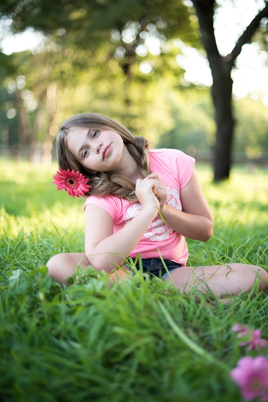 Toddler Photography: Young girl sitting in the grass with a big daisy behind her ear.