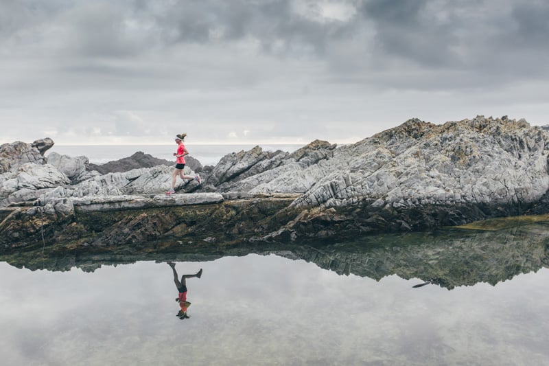 a beautiful shot of a runner. The skies are grey and her reflection shimmering in the water