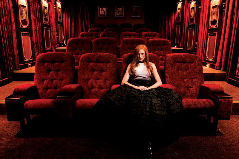 Dramatic photograph of a model with red hair sitting in a fiery red movie theatre
