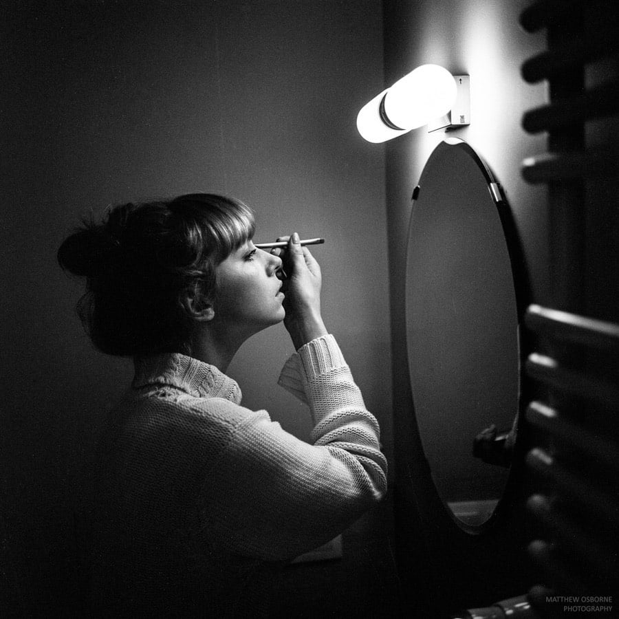 Black and white film photo of girl applying make-up by Matthew Osborne