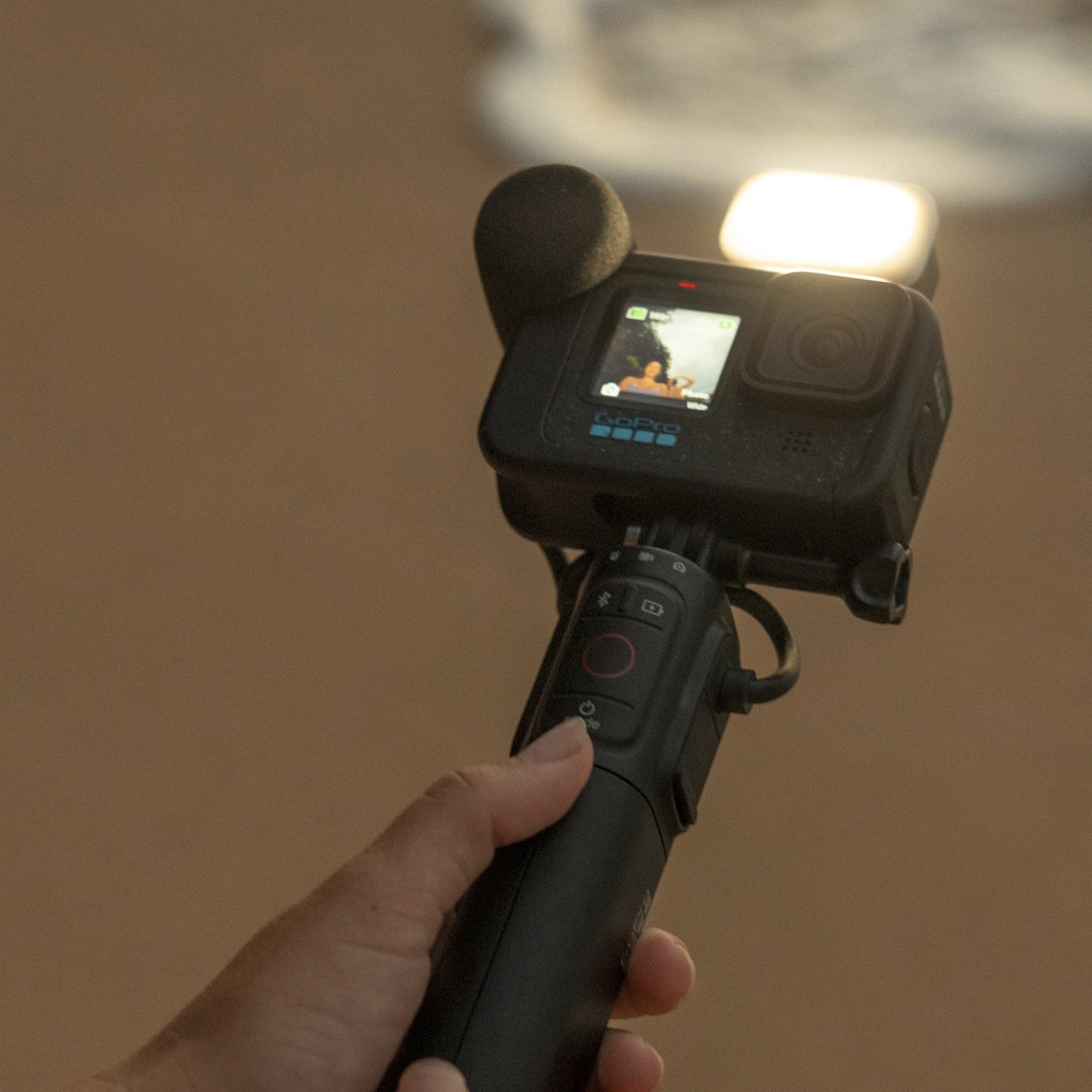 Hand holding a camera on a stick with a beach background