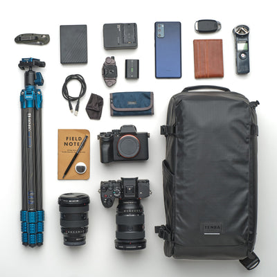 Collection of photography and travel gear including a camera, lenses, backpack, and accessories on a white background.