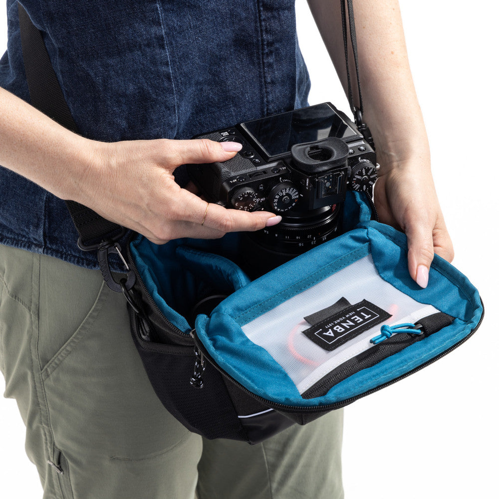 Person holding a camera and a blue carrying case with a camera inside, on a white background.
