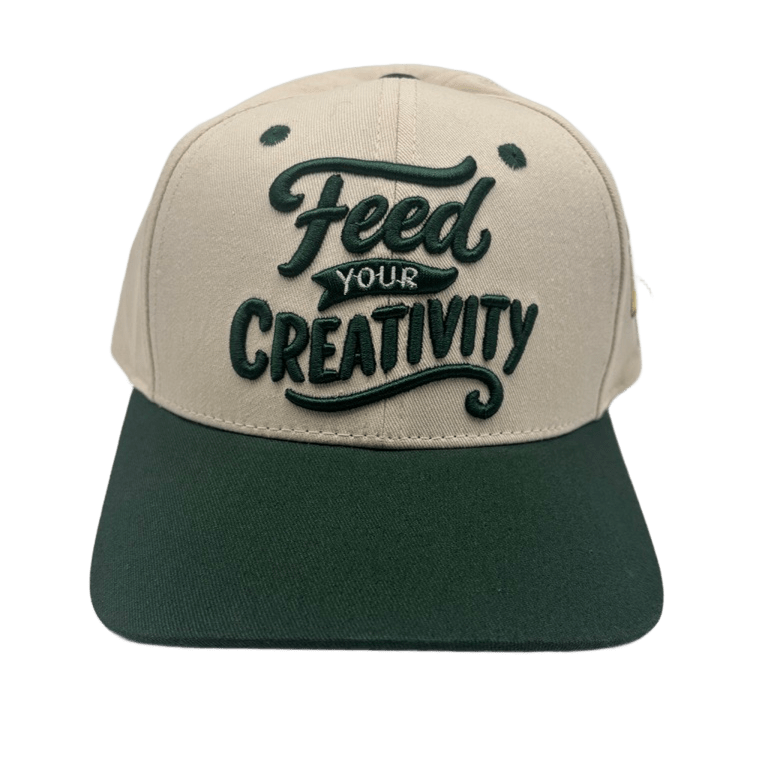 A two-tone baseball cap with a beige crown and a dark green flat brim, featuring the phrase 'Feed YOUR CREATIVITY' embroidered on the front in dark green.