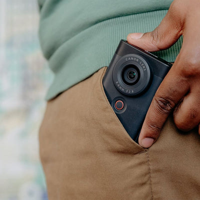Canon PowerShot V10 Vlog Camera in black, compact rectangular body with wide-angle lens, tilting flip-up screen, and built-in stand.