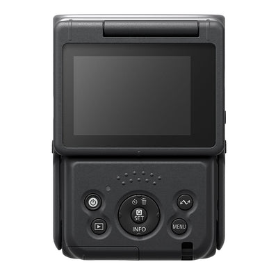 Canon PowerShot V10 vlog camera kit in silver — compact rectangular camera with wide-angle lens, flip-up screen, and integrated mini tripod stand.