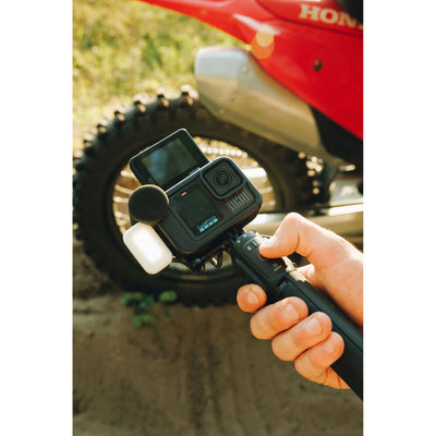 Action camera held by a hand with a dirt bike in the background