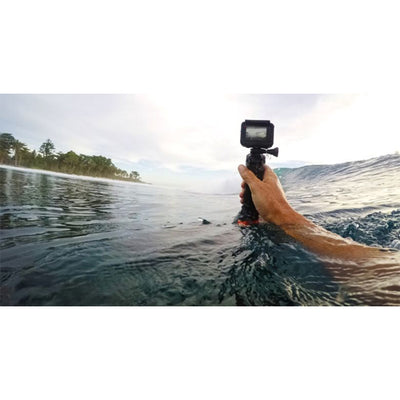 Hand holding a camera above water with a scenic background